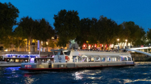 Bateau de croisière naviguant sur la Seine à Paris au crépuscule avec la ville illuminée en arrière-plan