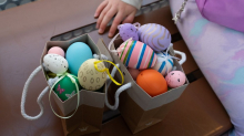 Dos bolsas llenas de huevos de Pascua decorados y coloridos sobre un banco, con la mano de un niño al lado.