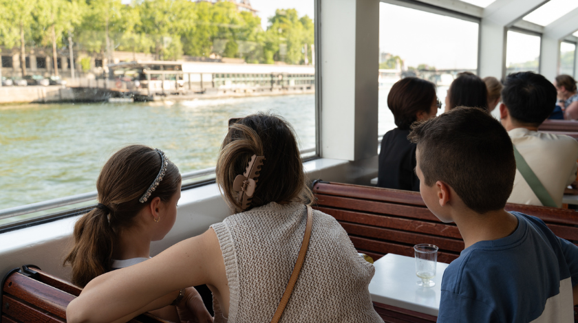 Famille avec enfants profitant d’une croisière sur la Seine à Paris, vue sur les quais depuis l’intérieur du bateau