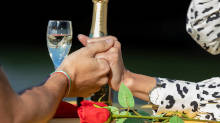 Instant romantique avec mains enlacées, rose rouge et champagne.