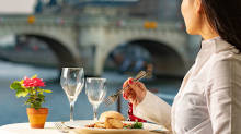 Woman enjoying dinner onboard with a view of a Parisian bridge