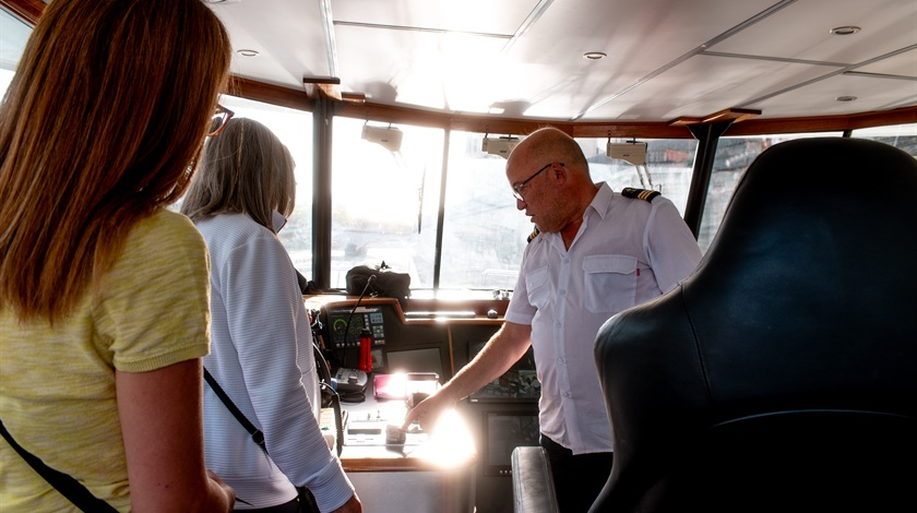 Un membre de l’équipage montre les commandes du bateau à deux visiteuses dans la cabine de pilotage.
