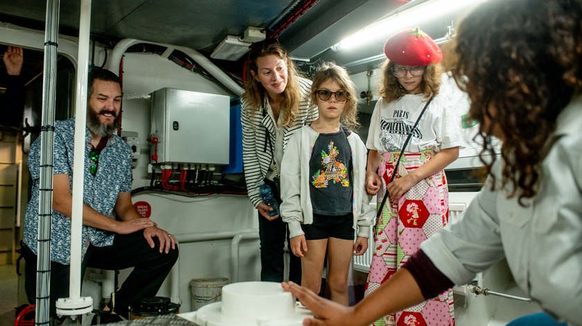 Une membre de l’équipage présente la salle des machines d’un bateau à deux adultes et deux enfants.