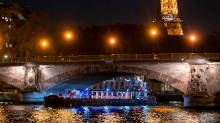 Barco de crucero acristalado pasando bajo un puente parisino con la Torre Eiffel iluminada al fondo